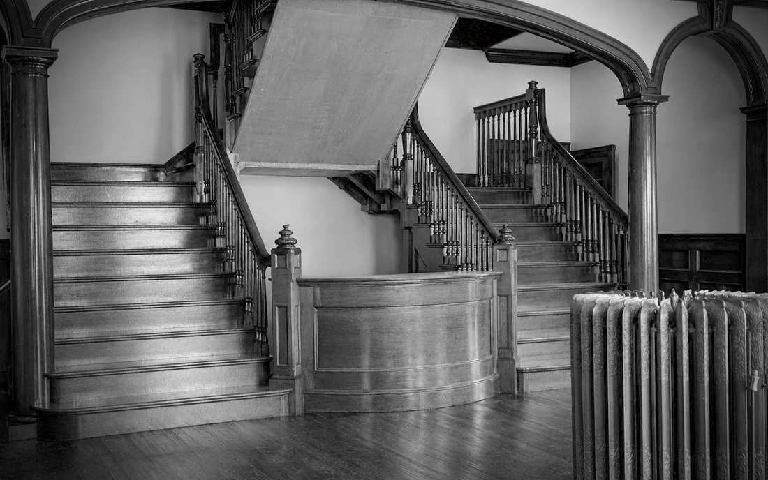 1903 entrance hall at Idylease in Newfoundland, New Jersey, showing the original front desk, staircase, arched openings, woodwork, and radiator