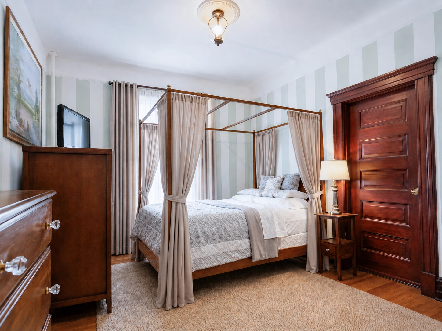 Guest room at Idylease with wood canopy bed, gathered floor-length bed curtains, full-length window drapery, striped walls, and original woodwork