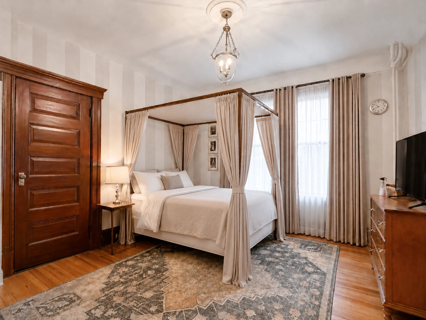 Guest room at Idylease with a four-poster canopy bed, floor-length curtains, tall windows, original wood door, and period woodwork